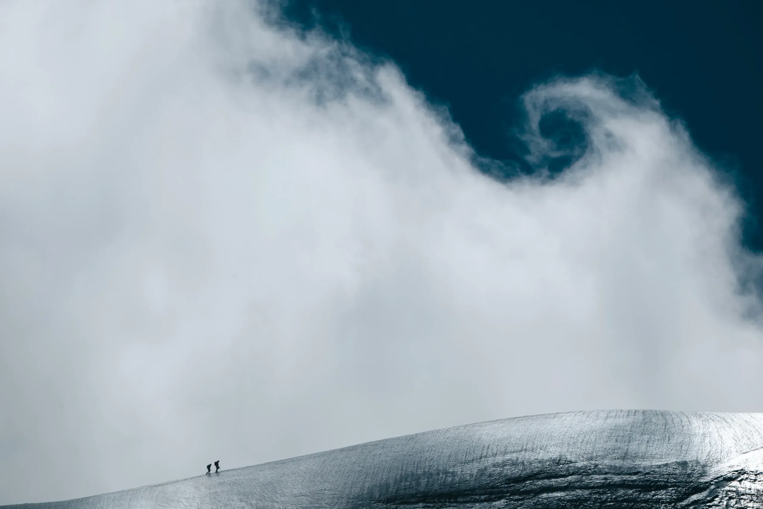 Zwei winzige Bergsteiger auf einem Schneehang unter einem Wolkenwirbel