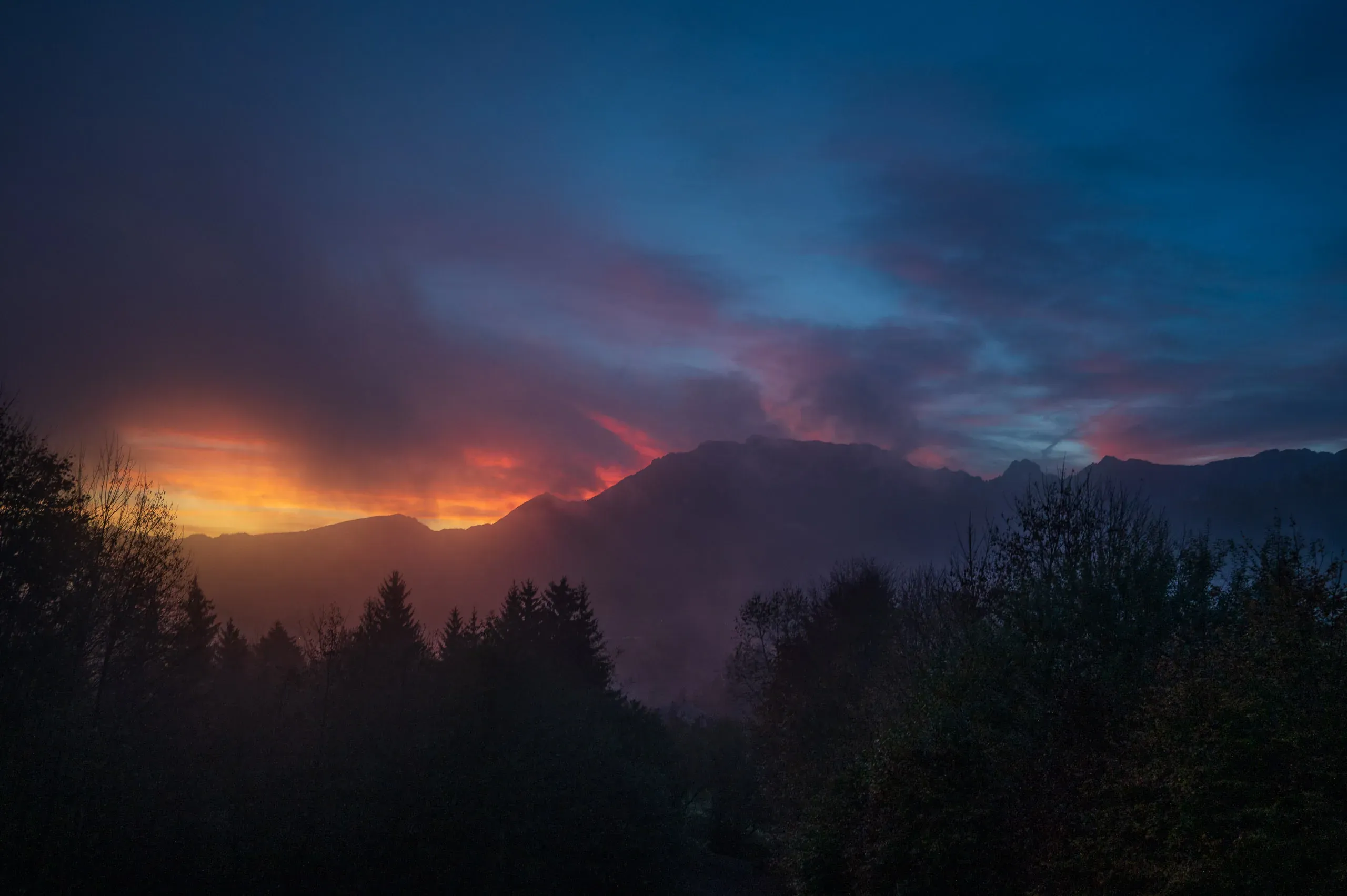 Feurig glühende Wolken über einer Bergkette mit Waldsilhouette
