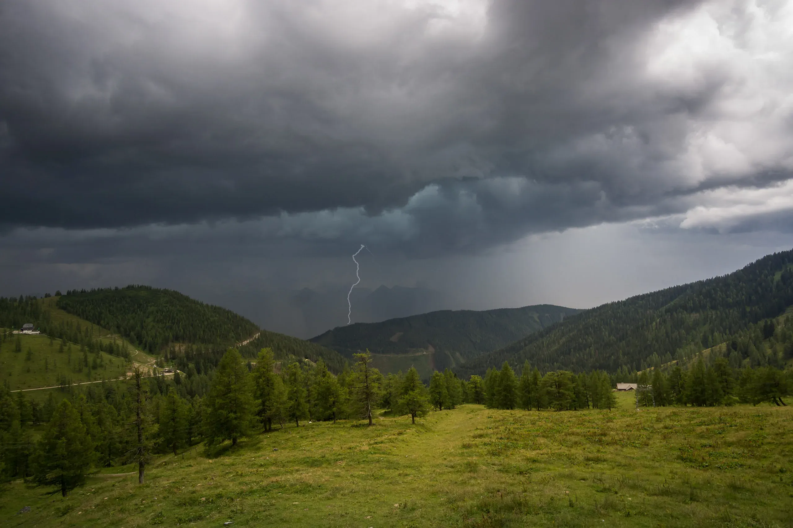 Ein Blitz entlädt sich unter dunklen Gewitterwolken über einem Almtal