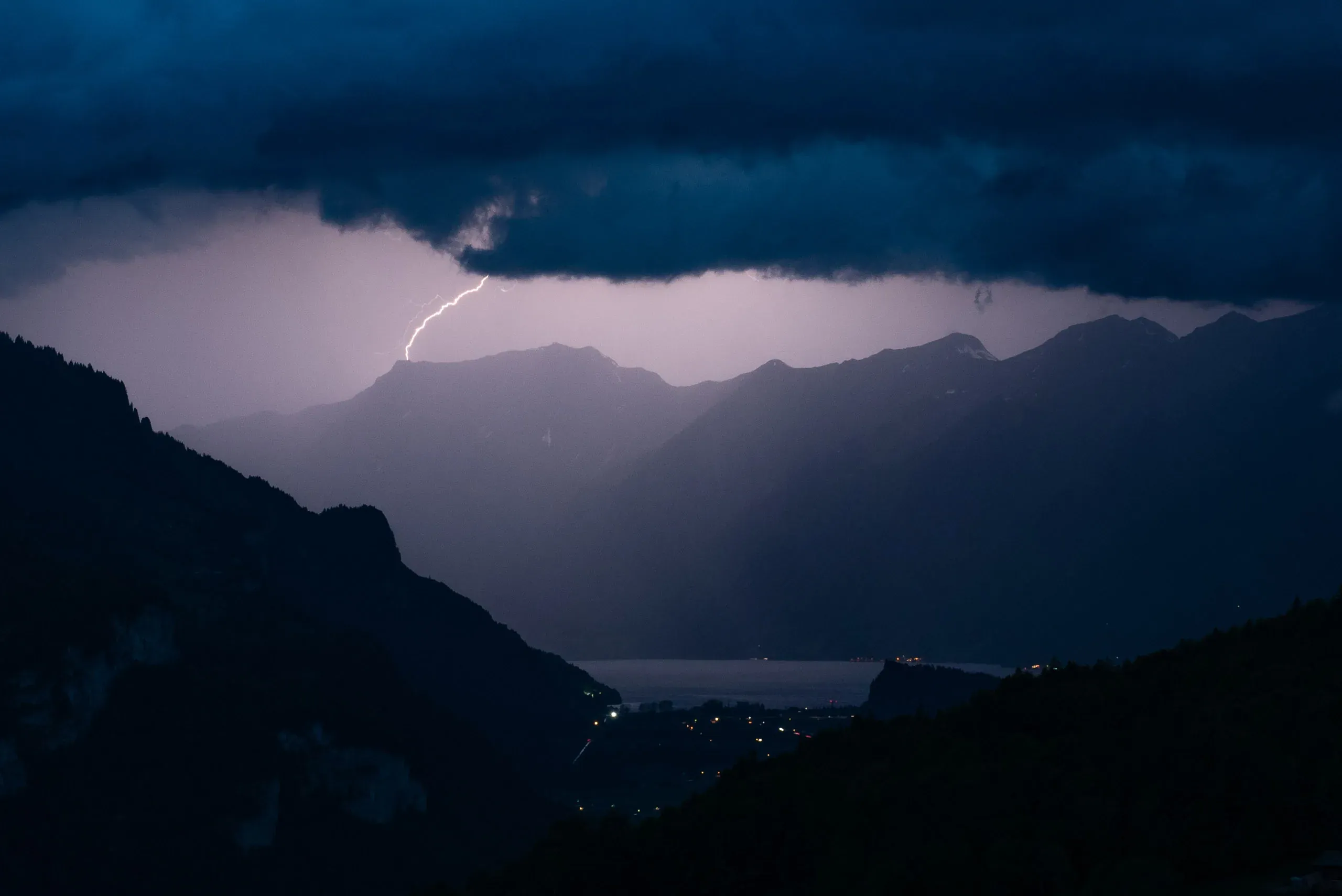 Blitz entlädt sich über einem Bergsee in der Dämmerung