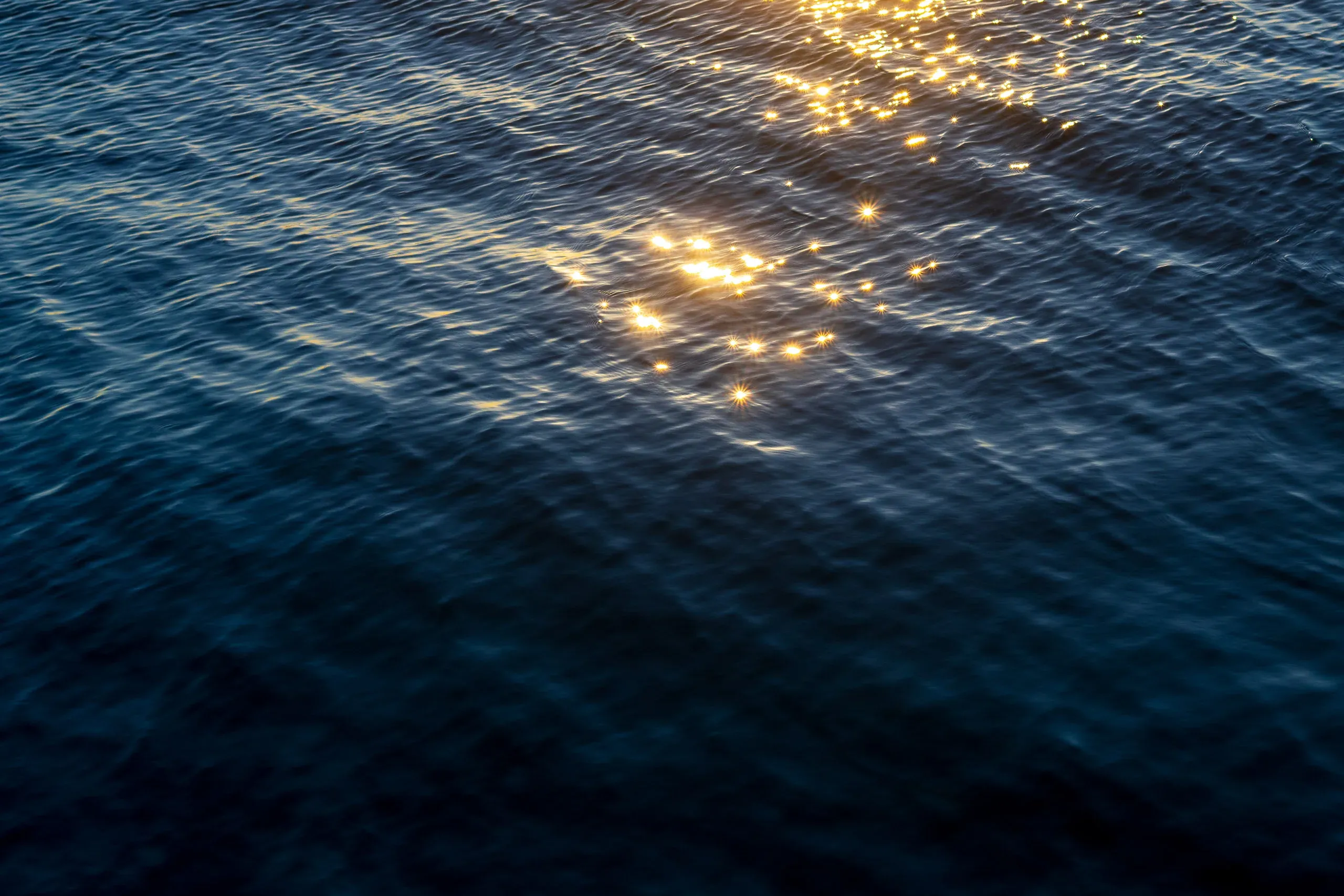 Goldene Lichtreflexe glitzern auf dunkler Wasseroberfläche