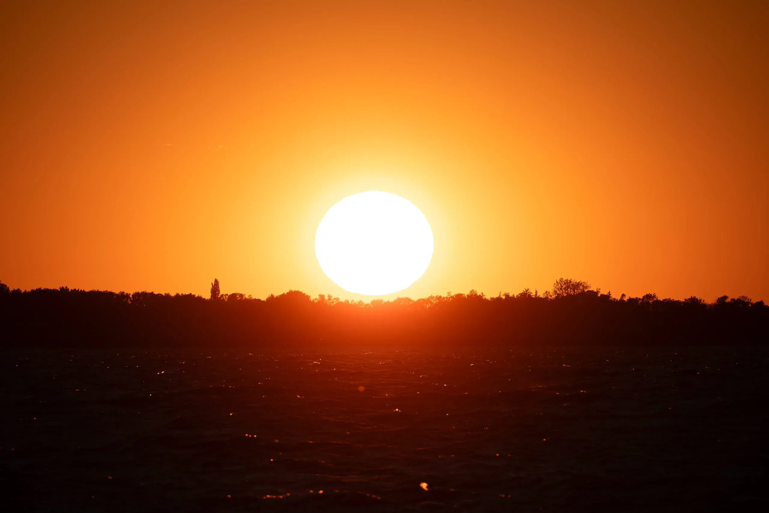 Glutrote Abendsonne sinkt über einer Uferlinie in den See