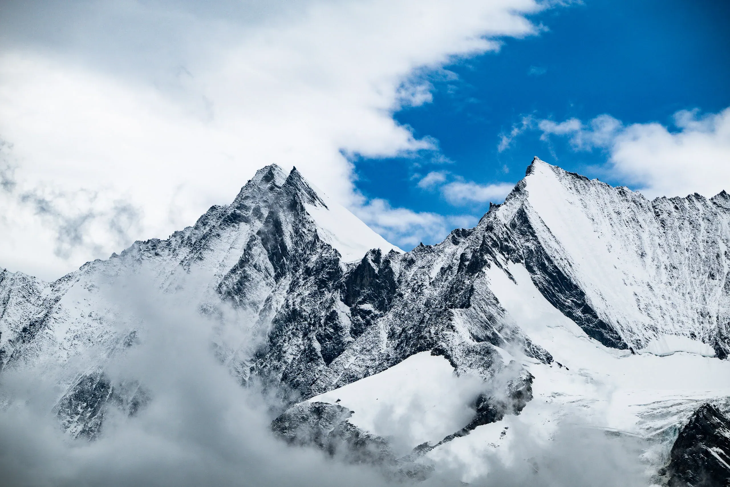 Verschneite Berggipfel mit Wolken vor blauem Himmel